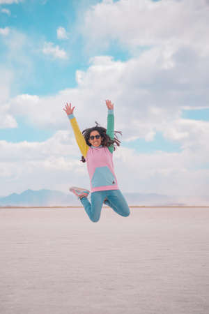 Young woman jumping and playing in a salt lake, with celestial sky and radiant sunの写真素材