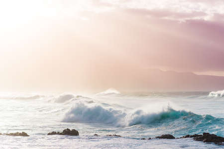 Beautiful Tropical Island Paradise Photo of Clear Aqua Blue Ocean Wave Crashing on Rocks with Sun Rays Coming Though Clouds of Colorful Pastel Sunset Sky at Dusk on Maui Hawaiiの写真素材
