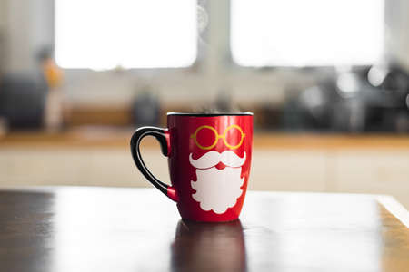 Cute Festive Holiday Photo Of Bright Red Seasonal Santa Christmas Coffee Mug with Hipster Beard and Hot Steam Coming Off Cup in Light White Modern Kitchen Such a Warm Cozy Morningの写真素材