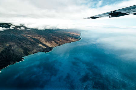 Scenic Aerial View of Clear Blue Ocean Water and Tropical Island with Clouds and Airplane Wing
