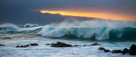 A panoramic shot of a stormy ocean wave during a sunset