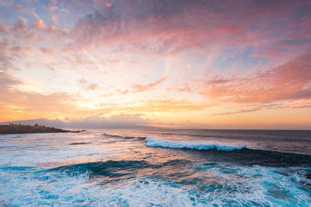 Beautiful Tropical Island Paradise Aerial Photo of Clear Aqua Blue Ocean Water with Waves Crashing on Rocks with Sun Rays Coming Though Clouds of Colorful Pastel Sunset Sky at Duskの写真素材