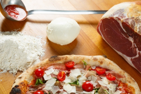 Typical Italian Pizza cooked in electric oven with ingredients in the background on a wood tableの写真素材