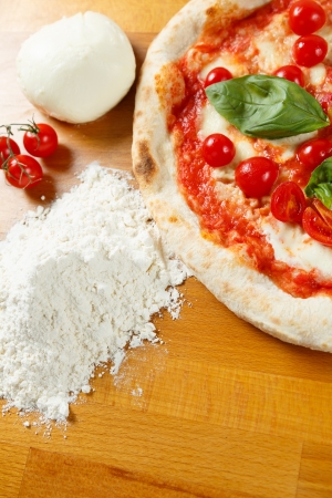 Typical Italian Pizza cooked in electric oven with ingredients in the background on a wood tableの写真素材