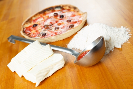 Typical Italian Pizza cooked in electric oven with ingredients in the background on a wood tableの写真素材