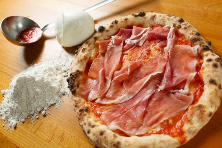 Typical Italian Pizza cooked in electric oven with ingredients in the background on a wood tableの写真素材