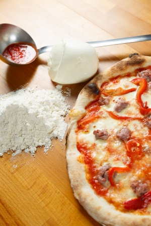 Typical Italian Pizza cooked in electric oven with ingredients in the background on a wood tableの写真素材