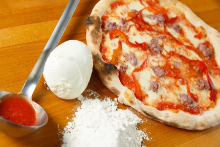 Typical Italian Pizza cooked in electric oven with ingredients in the background on a wood tableの写真素材