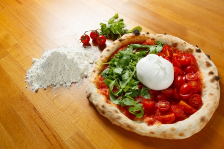 Typical Italian Pizza cooked in electric oven with ingredients in the background on a wood tableの写真素材