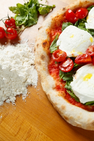 Typical Italian Pizza cooked in electric oven with ingredients in the background on a wood tableの写真素材