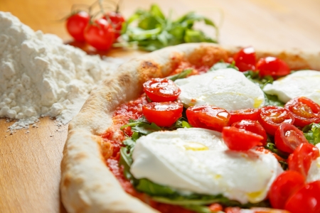Typical Italian Pizza cooked in electric oven with ingredients in the background on a wood tableの写真素材