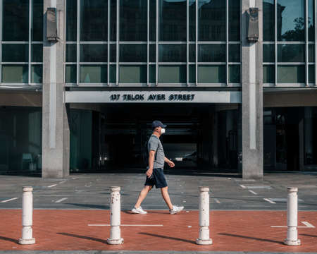 Man with a face mask walking along a street in sunny Central Singapore during the pandemic period.のeditorial素材