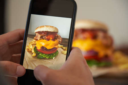 unrecognizable man taking a picture of a delicious burger with his phone. Food concept