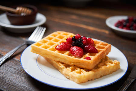 Fresh waffles on a plate with berries and honey on a wooden table. Copy space. Front view