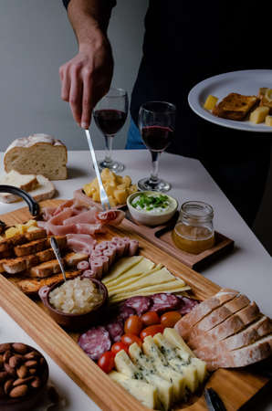 Delicious Charcuterie Board with snacks cheese, toast, ham, blue cheese, almonds, caramelized onions, green onion, honey, toast. Flat-lay view. Family, friends holiday gathering. Argentine Tradition. Picada. Unrecognizable Man holding a plate and taking food.の写真素材