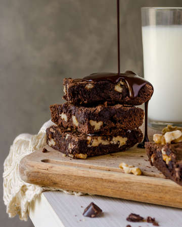 A stack of chocolate brownies with nuts and melting chocolate on a wooden tableの写真素材