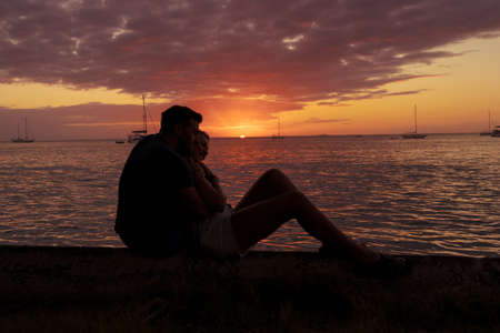 Young couple in love hugging watching the sunset by the sea on their relaxing vacation away from routine. Life style conceptの写真素材