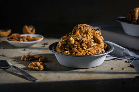 Ice cream with chocolate, nuts and almonds served in metal bowl on wooden tableの写真素材