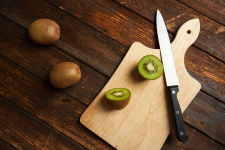 One kiwi fruit cut in halves and two whole kiwi fruit with a knife on wooden table and background.の写真素材