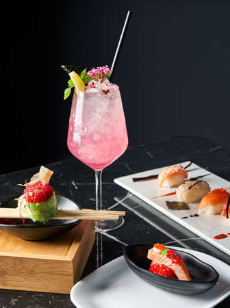 General view of table with a refreshing drink, white plate of sushi pieces in the black background. Front view. Food conceptの写真素材