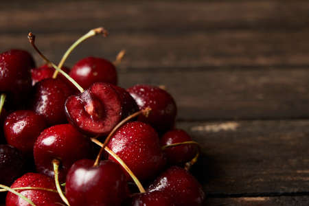 Close up of pile of sweet red cherries with stalks and leaves on a wooden table. Black background. Food and fruit concept. Space for your textの写真素材