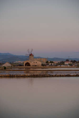 Landscape of salt pans in traditional salt production with mountain of Erice in background in Trapani, Sicily, Italy, historical architecture like water lifting mill, old barrages and ponds with sea water. Salt works in Sicily Island.の写真素材