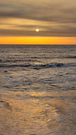 Closeup sea sand beach. Panoramic beach landscape. Beach seascape horizon with a beautiful sun in front. Orange and golden sunset relaxing sunlight. Vacation travel holiday. Summer mood. Sunset in Sicily, Italyの写真素材