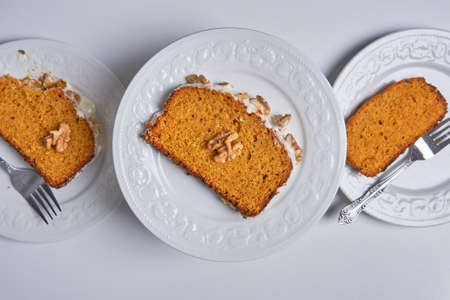 Slices of homemade carrot cake with sugar glaze and walnuts served in three white dishes. Food conceptの写真素材
