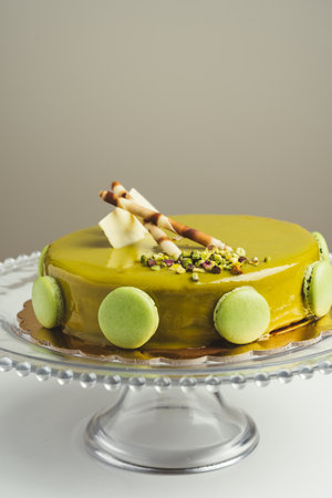 delicious homemade cake with pistachio macarons and wafers on top in a glass cake plateの写真素材