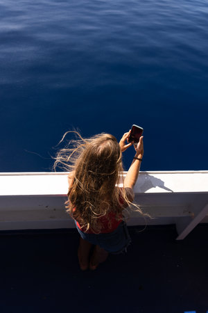 Young blonde tourist taking selfie with her smartphone on a ferryboat.