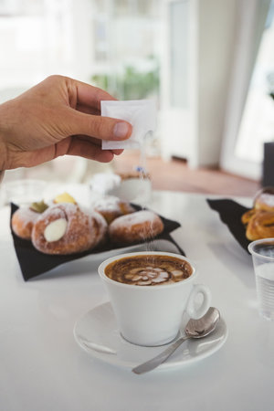 unrecognizable man pouring sugar into a cup on a white table at a coffee shopの写真素材