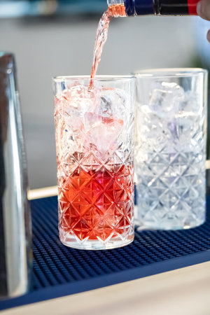 Bartender pouring alcohol from the bottle preparing a fresh cocktail. Close-up.