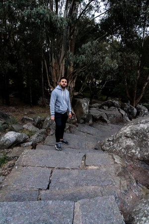 A man in a hoodie walks along a rugged stone trail surrounded by trees and rocks. Perfect for themes...
