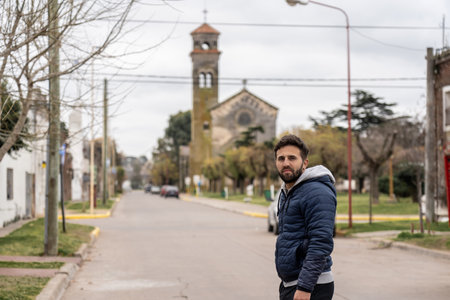 Man smiling on a quiet street in a small Argentine town, with a historic church and colonial architecture in the background on a cloudy winter day.の写真素材