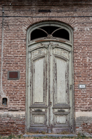 A rustic wooden door set in a red brick wall with visible aging and a broken window panel.の写真素材