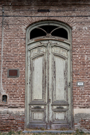A rustic green wooden door set in a red brick wall with visible aging and a broken window panel.の写真素材