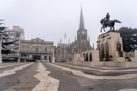 Foggy view of Independence Square in Azul featuring a historic church and equestrian monument. A blend of architecture, history, and culture.の写真素材