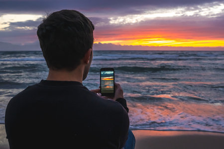 Man taking photo of colorful ocean sunset with smartphone