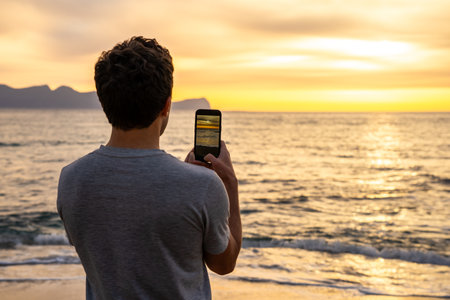 Man taking picture of golden sea sunset with smartphone on the beach