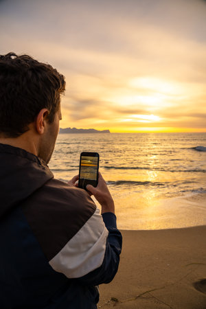 Man taking picture of golden sea sunset with smartphone on the beach
