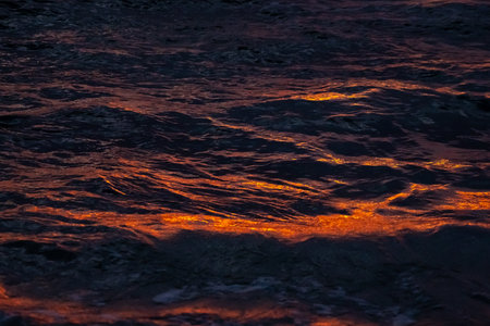 Colorful ocean waves at sunset with rocks on the sandy shore