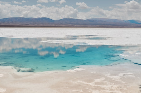 Scenic view of a salt flat with a turquoise pool and mountains in the background