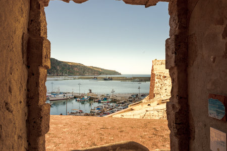 Mediterranean harbor seen through old stone wall windowの写真素材