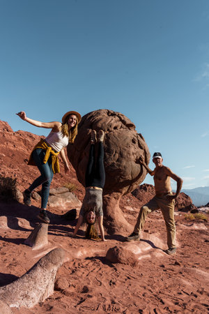 Group of people playfully interacting with a giant rock in a red desert setting