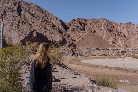 Young woman standing in arid mountain landscape with pyramid-shaped hill in the backgroundの写真素材