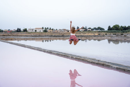 Woman jumping at salt flats with pink reflectionの写真素材
