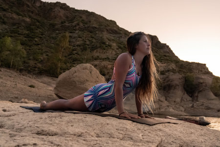 Woman practicing cobra pose on rock by lake at sunset
