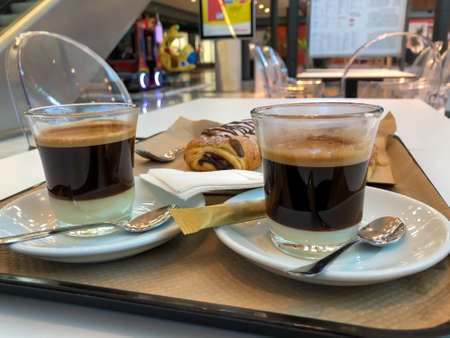 Close-up of two coffee glasses and chocolate deserts over a tray in a shopping centerの写真素材