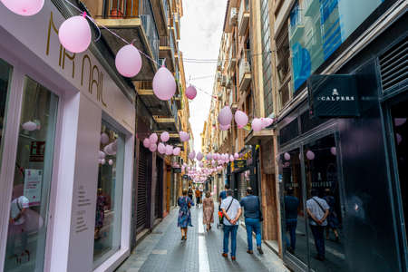 Murcia, Spain - October 16, 2021: Downtown Murcia street decorated with pink balloons for the day of fight against cancer. People walking and looking at the shop windows.のeditorial素材