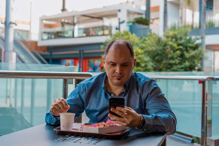 A young man is sitting at a table having breakfast and looking at his mobile.の写真素材